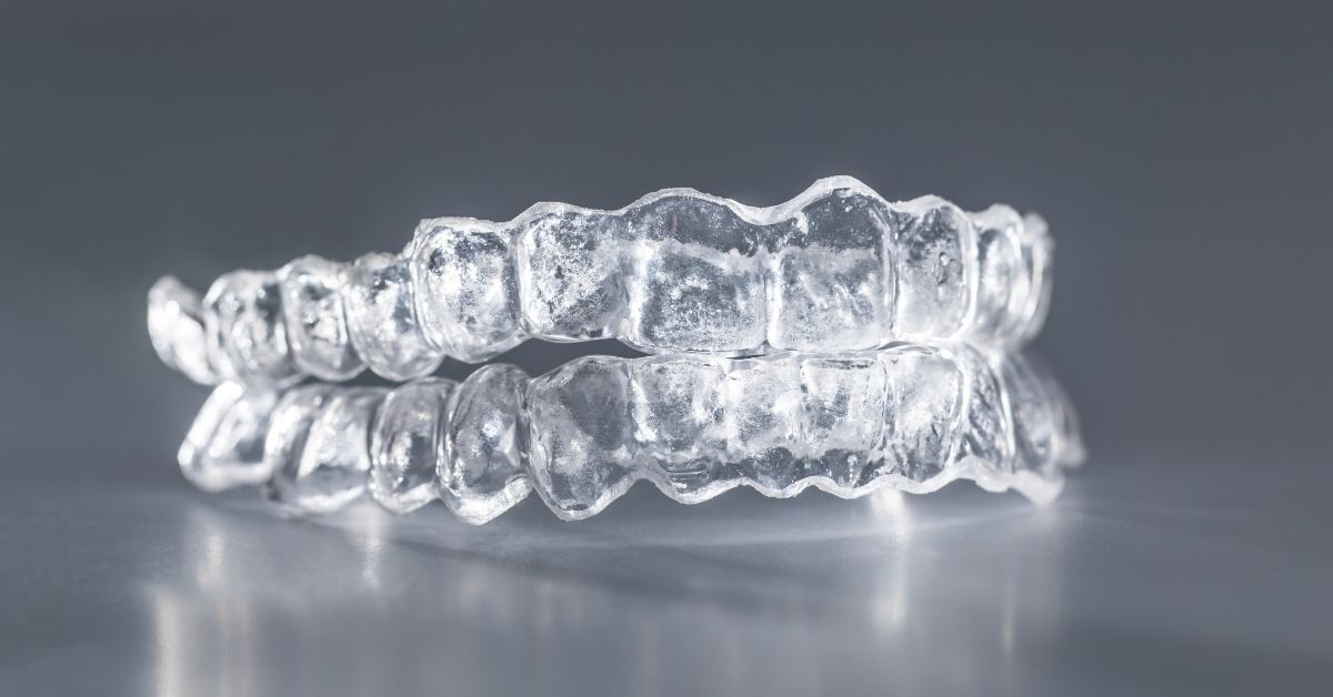Close-up of clear Invisalign aligners on a reflective surface, representing modern orthodontic technology for discreet teeth straightening.